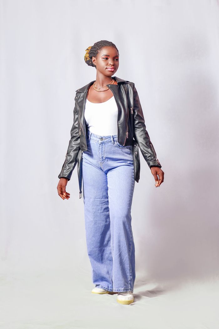 Stylish young woman in denim and leather jacket posing in studio setting.
