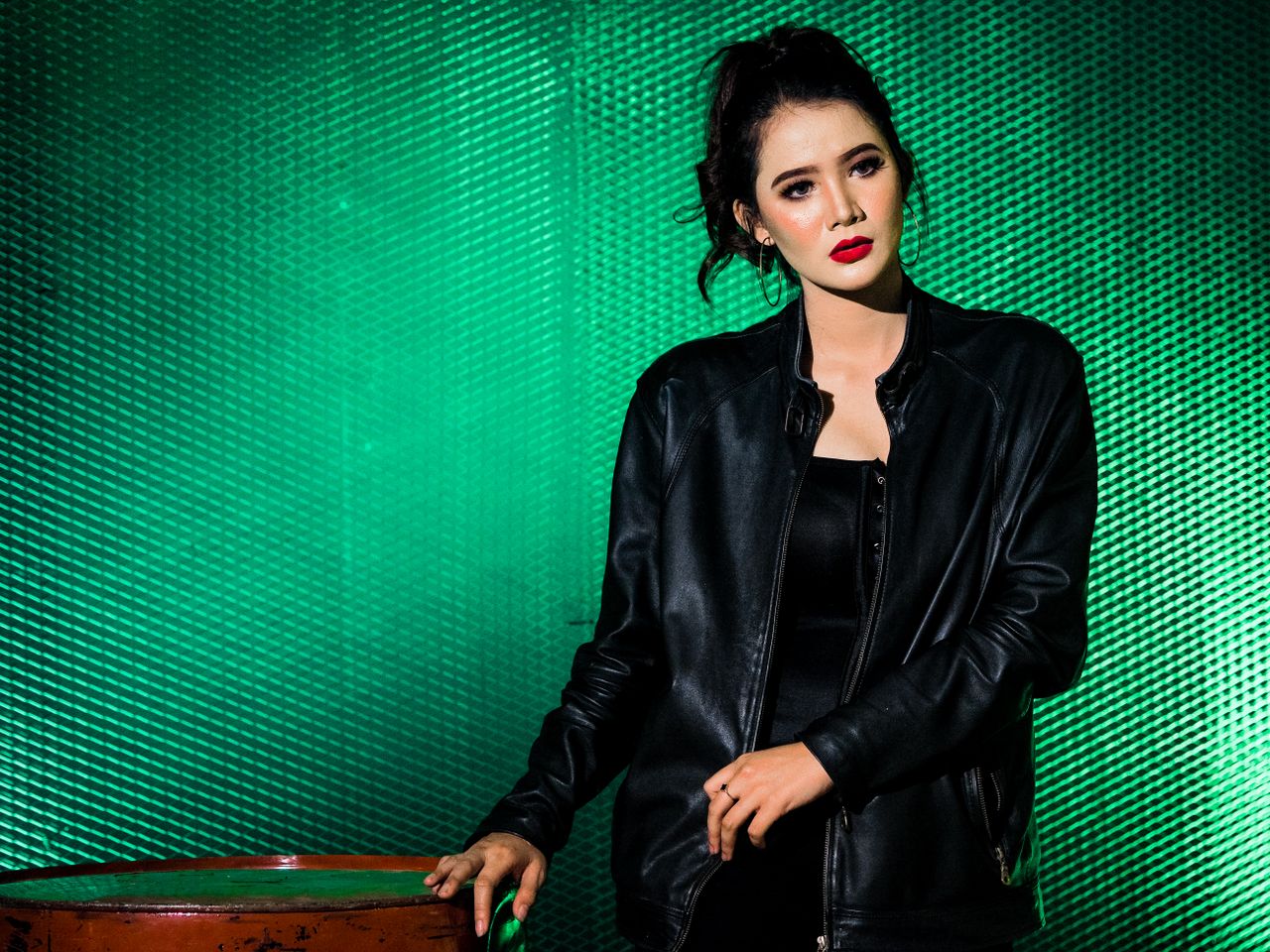 Portrait of a fashionable woman in a black leather jacket with red lips against a green background.