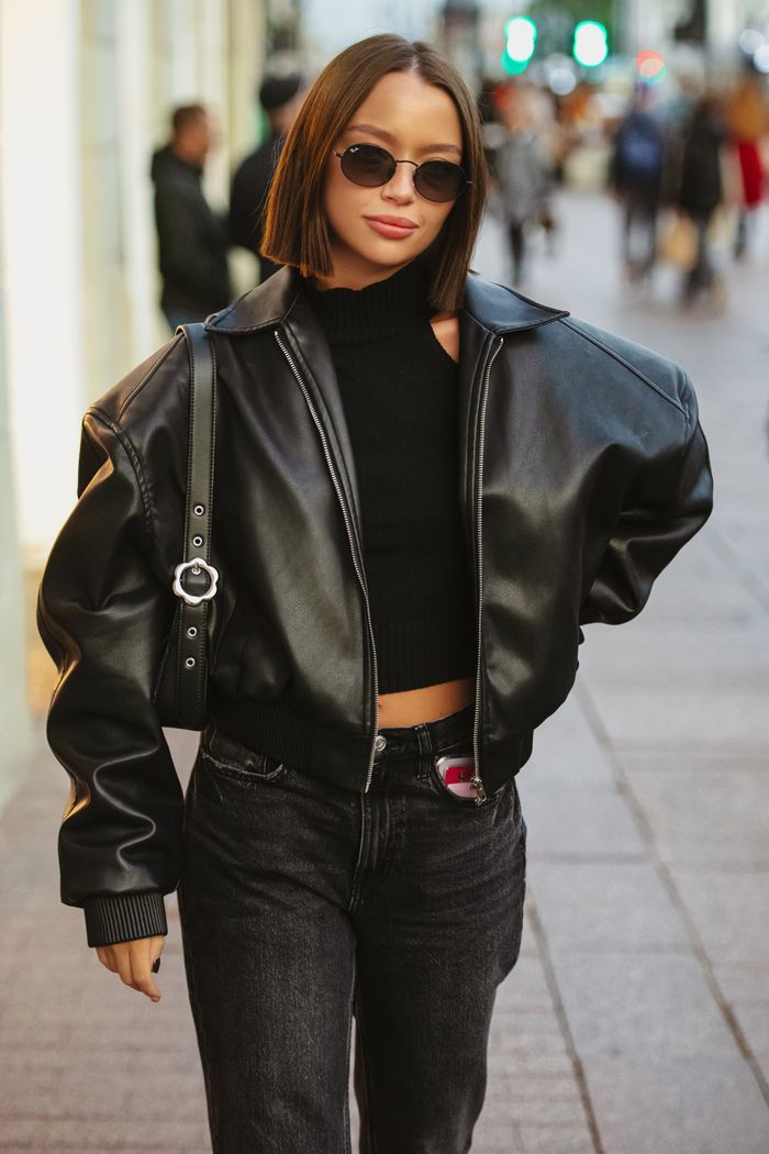 Stylish woman in leather jacket struts confidently along bustling urban street.