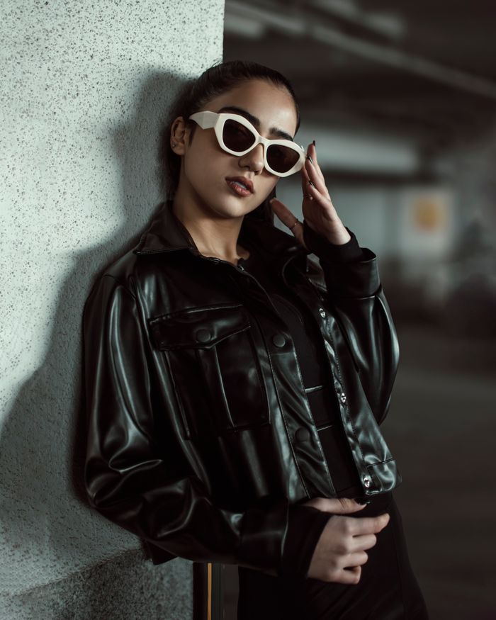 Fashionable woman in black leather leaning on a wall, exuding confidence.