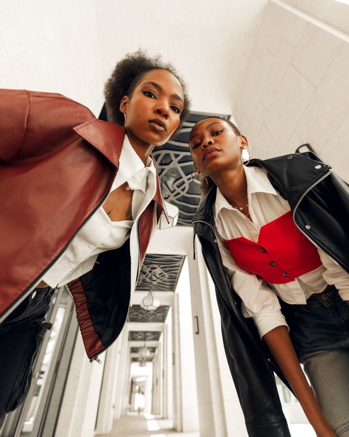 The Art of Drawing Readers In: Your attractive post title goes here Two stylish women in modern attire pose confidently in an architectural corridor, showcasing bold fashion choices.